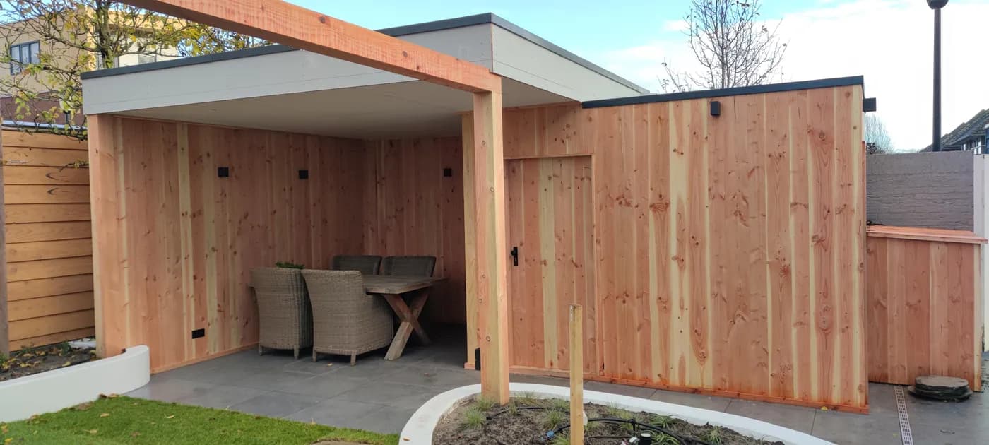 Op maat gemaakte houten overkapping met een dichte wand en een zithoek eronder, aan een terras