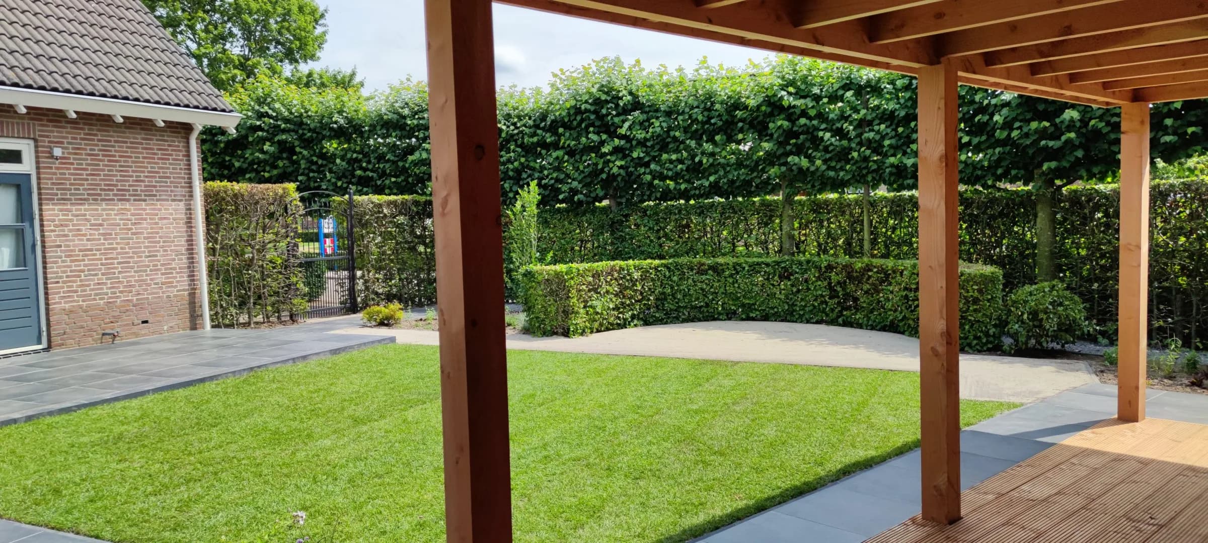 Door ons aangelegde tuin met een houten overkapping, strakke beukenhaag en een ruim gazon