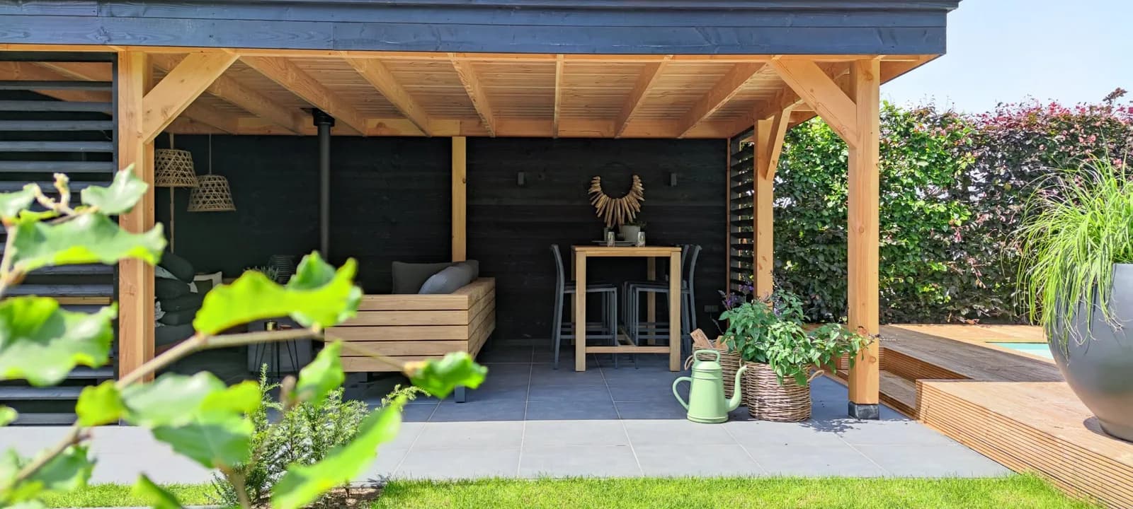 Houten overkapping met loungeset en bar, naast een vlonder en een strak gazon