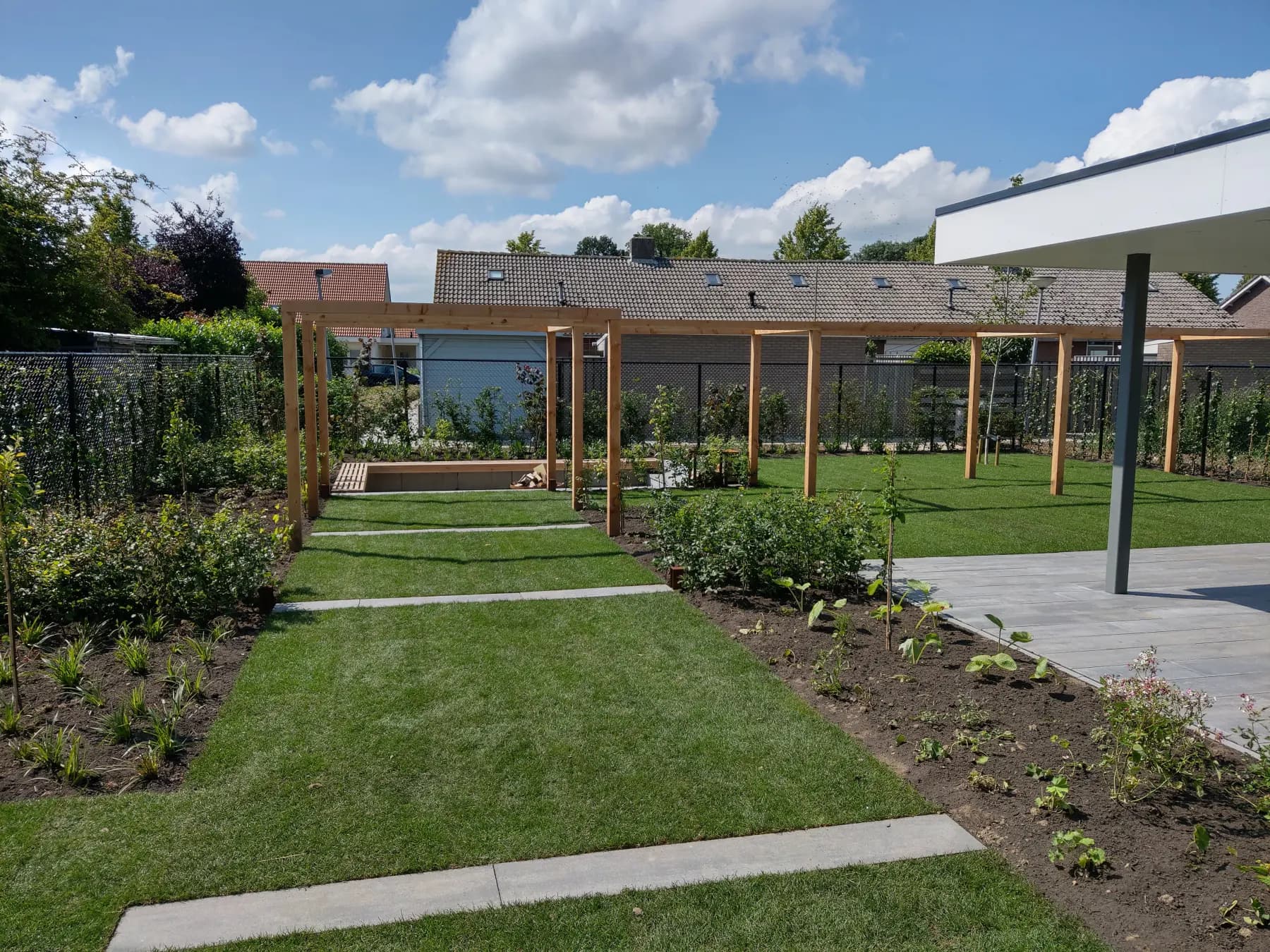 Lange tuin bij een nieuwbouwwoning met houten pergola, borders en gazon